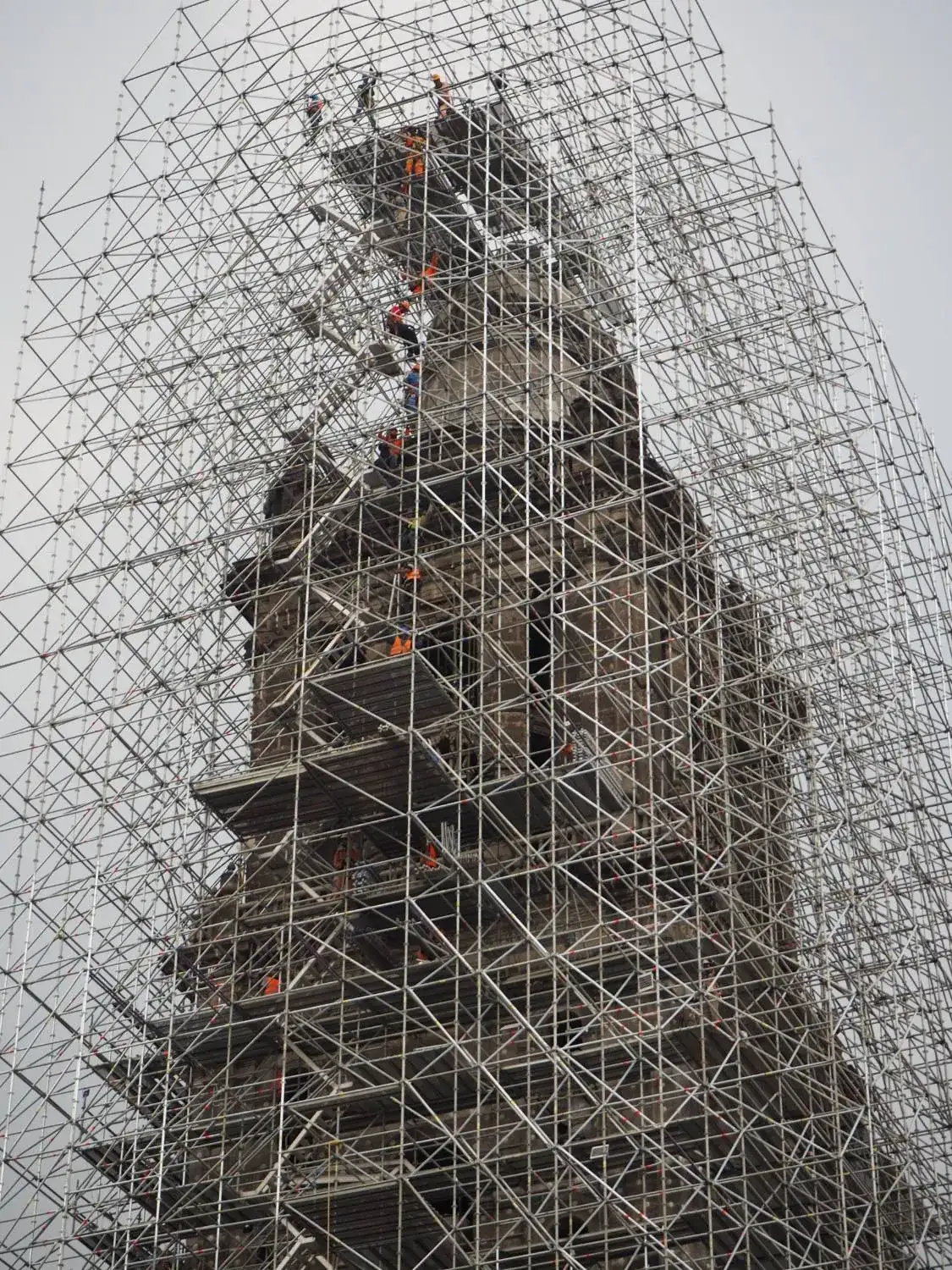 Menara tua yang diselubungi perancah, dengan pekerja berompi oranye di beberapa tingkat